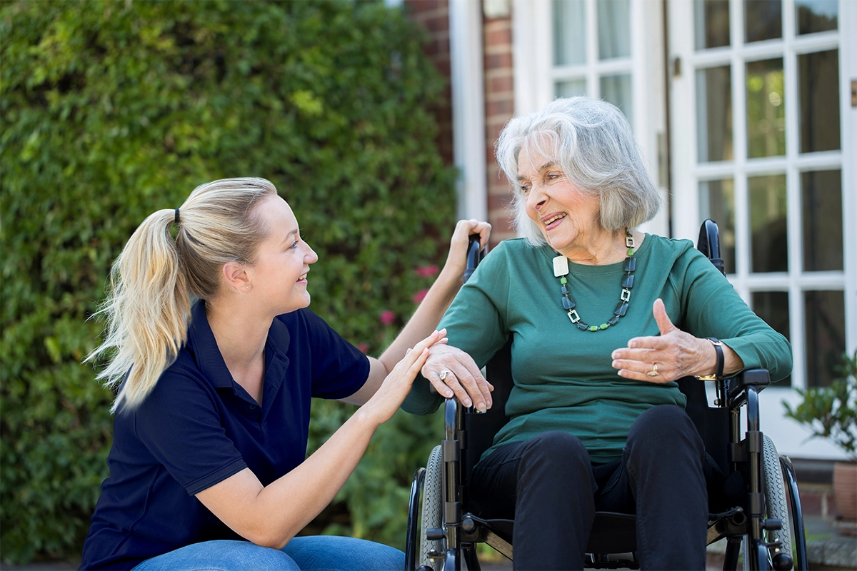 A-caring-live-in-carer-chatting-warmly-with-an-elderly-woman-in-a-wheelchair-outside-her-home-reflecting-companionship-dignity-and-quality-home-care